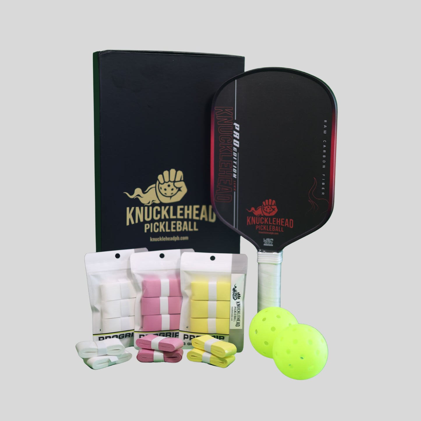 Knucklehead Pickleball gift set featuring a black paddle, black box, two neon yellow pickleballs, and pink and yellow wristbands on a light gray background.