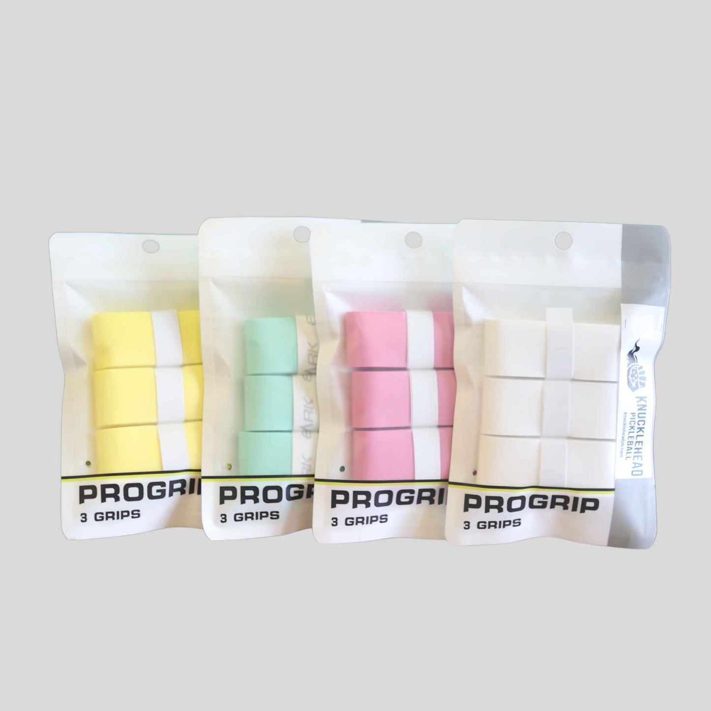Four packages of PROGRIP golf grips in pastel yellow, mint green, pink, and white, arranged in a row against a solid gray background.