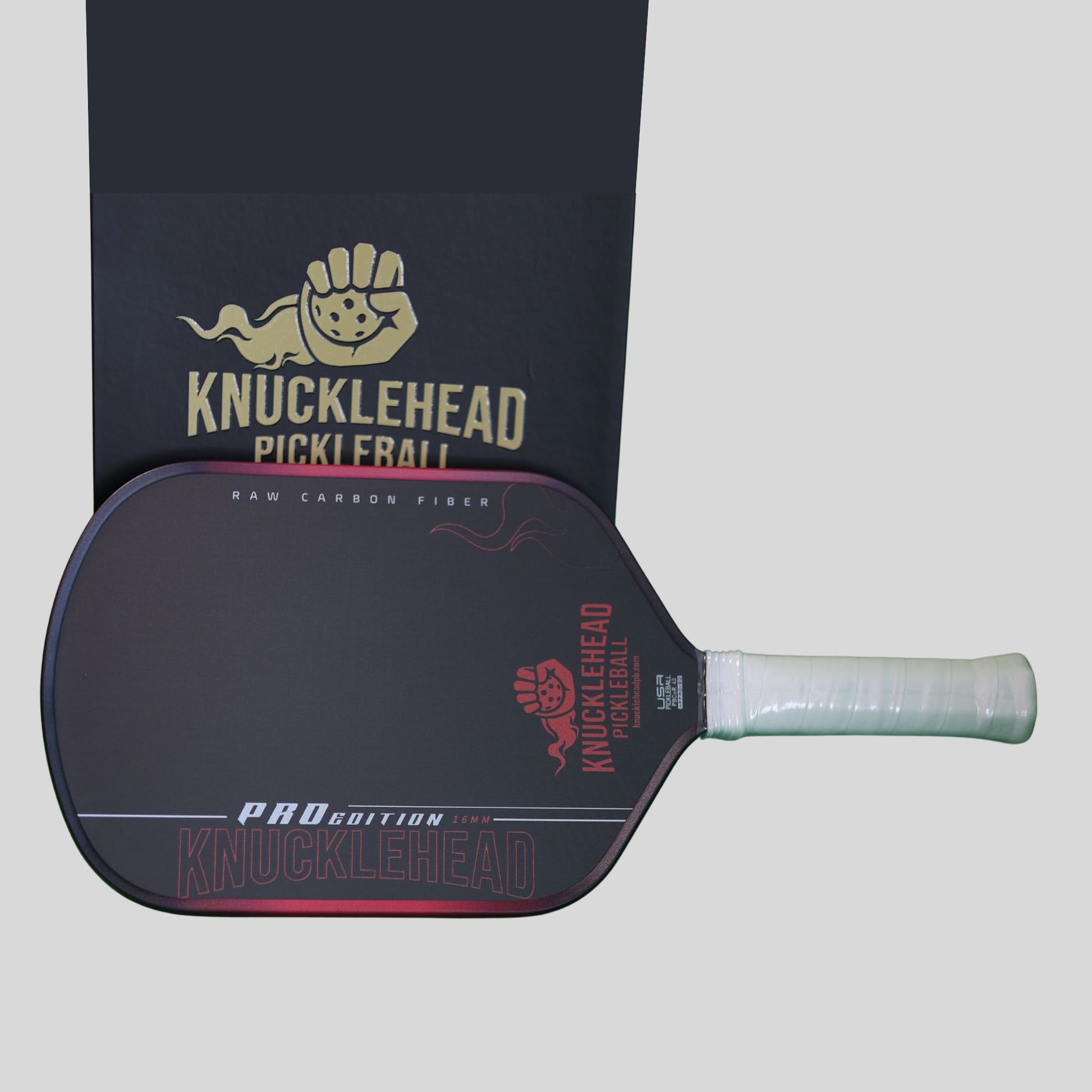 Knucklehead Pro Edition Raw Carbon Fiber pickleball paddle with a light green grip, shown in front of its black branded packaging box on a light gray background.