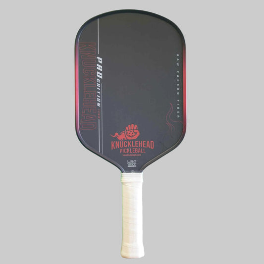 A Knucklehead pickleball paddle with a black face, red and white branding, and a white wrapped handle, shown against a solid gray background.